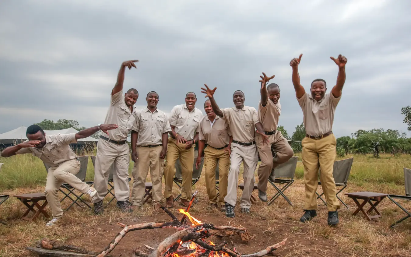 Safari guides celebrating around campfire in grassland camp, Serengeti North Wilderness Camp, Serengeti National Park, Tanzania