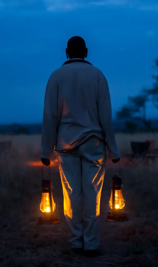 Person holding lanterns standing in savanna grassland at dusk, Serengeti North Wilderness Camp, Serengeti National Park, Tanzania