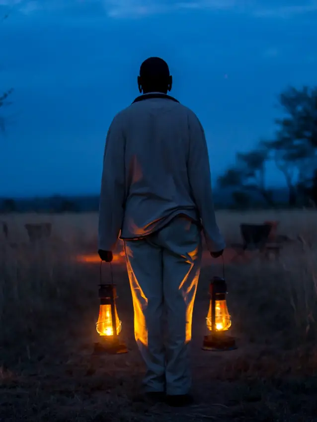 Person holding lanterns standing in savanna grassland at dusk, Serengeti North Wilderness Camp, Serengeti National Park, Tanzania