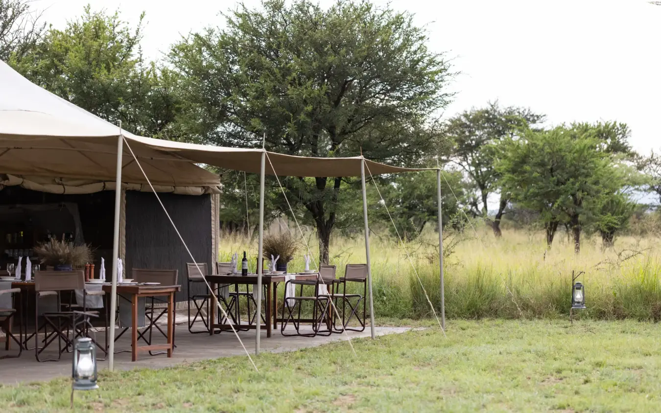 Safari camp dining area with canvas tent and outdoor seating in grassland, Serengeti Wilderness Camp, Serengeti National Park, Tanzania