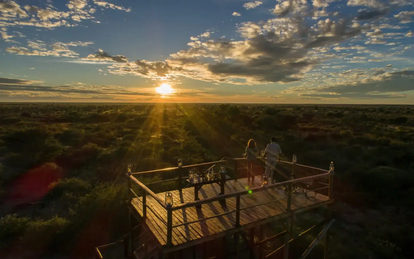 Guests on wooden deck overlooking savanna at sunset, Shinde, The Okavango Delta, Botswana