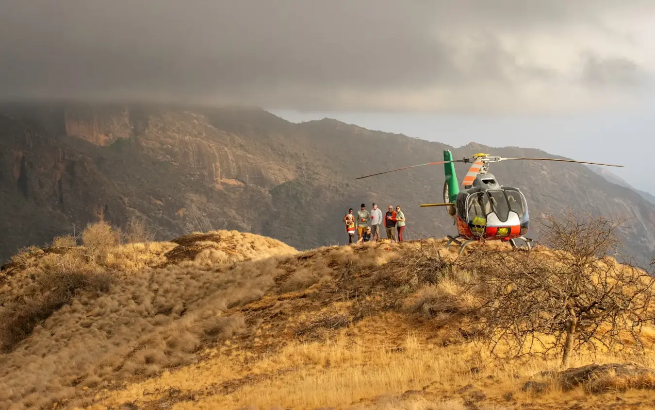 Helicopter landing on rocky hillside with group of people waiting, Suyian Lodge, Laikipia Highlands, Kenya