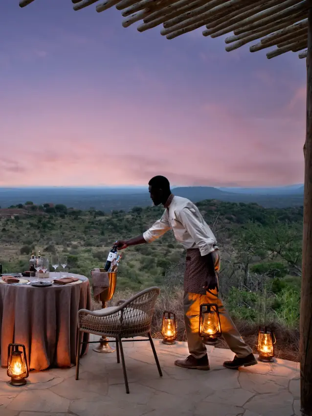 Server pouring wine at outdoor dining setup overlooking savanna landscape at dusk, Suyian Lodge, Laikipia Highlands, Kenya