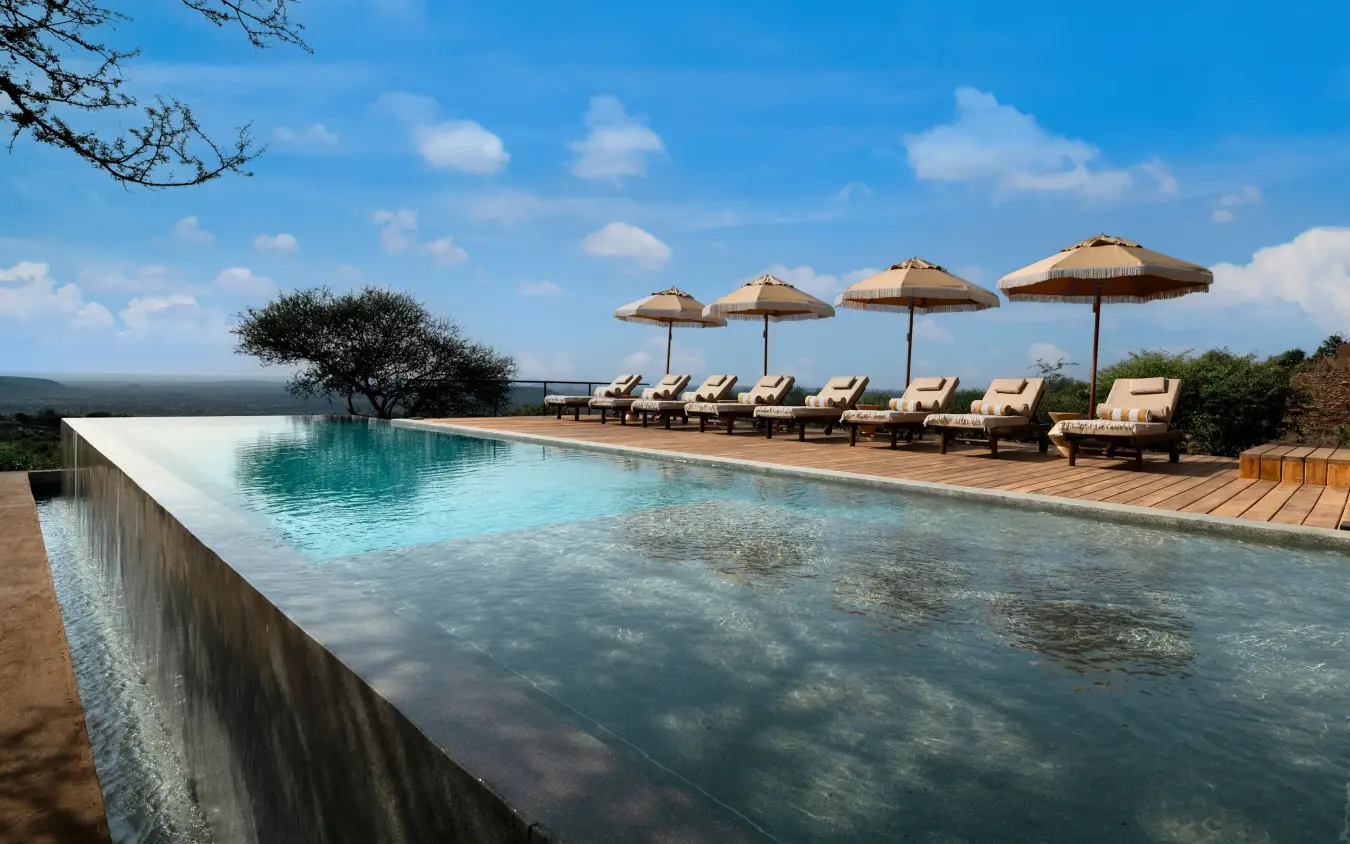 Infinity pool with loungers and umbrellas overlooking savanna landscape, Suyian Lodge, Laikipia Highlands, Kenya