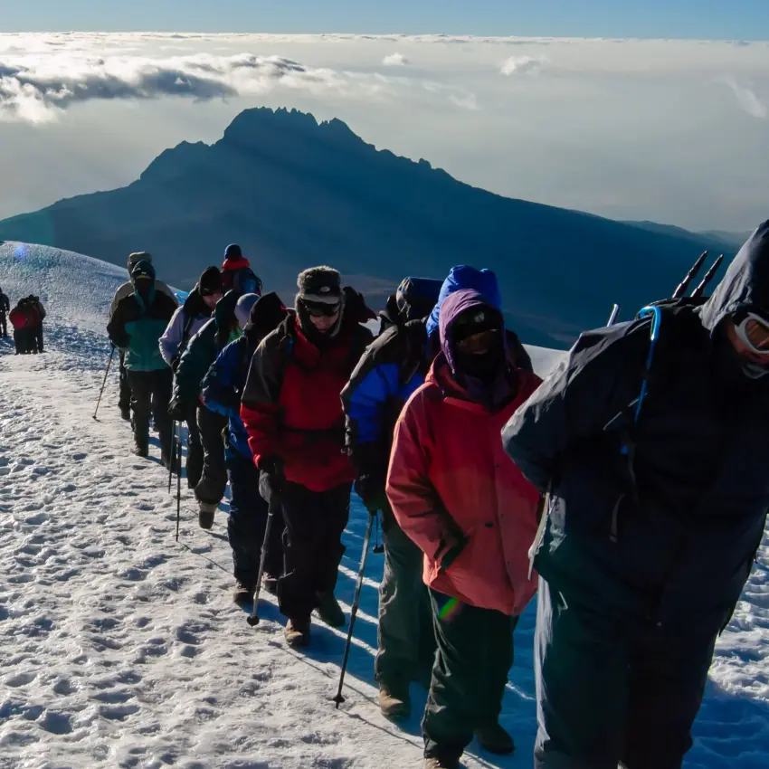 line of trekkers ascending snow-covered ridge on Kilimanjaro above the clouds