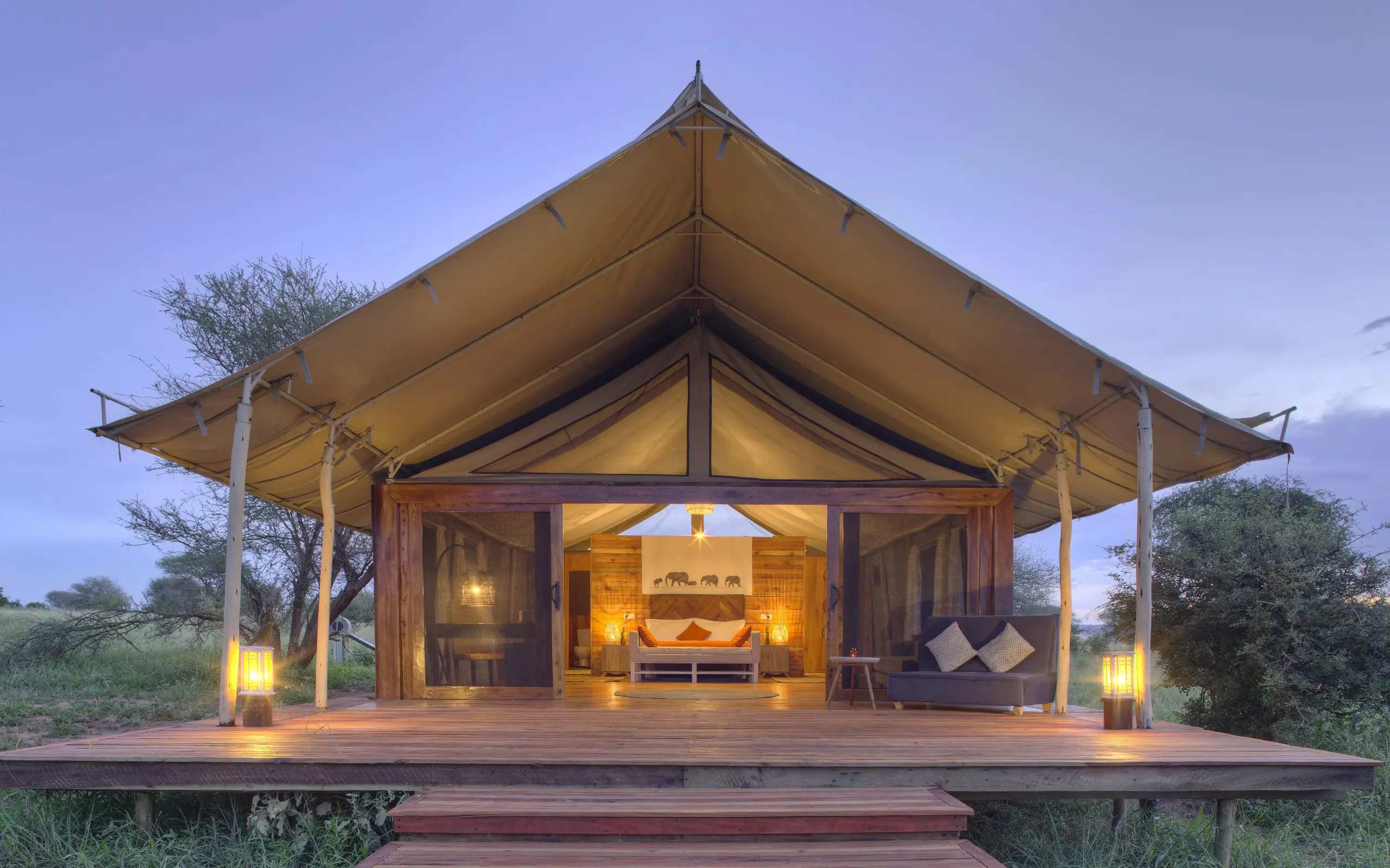 Luxury canvas tent with wooden deck lit up at dusk in savanna landscape, Tarangire Ndovu Tented Lodge, Tarangire National Park, Tanzania