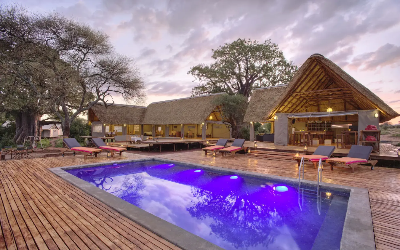 Luxury lodge with illuminated pool at dusk surrounded by African savanna trees, Tarangire Ndovu Tented Lodge, Tarangire National Park, Tanzania