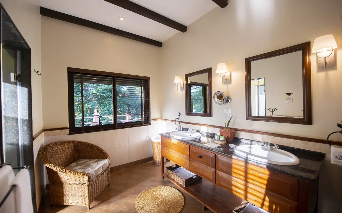Luxury bathroom with wooden vanity and wicker chair overlooking tree canopy, The Retreat at Ngorongoro, Ngorongoro Crater, Tanzania