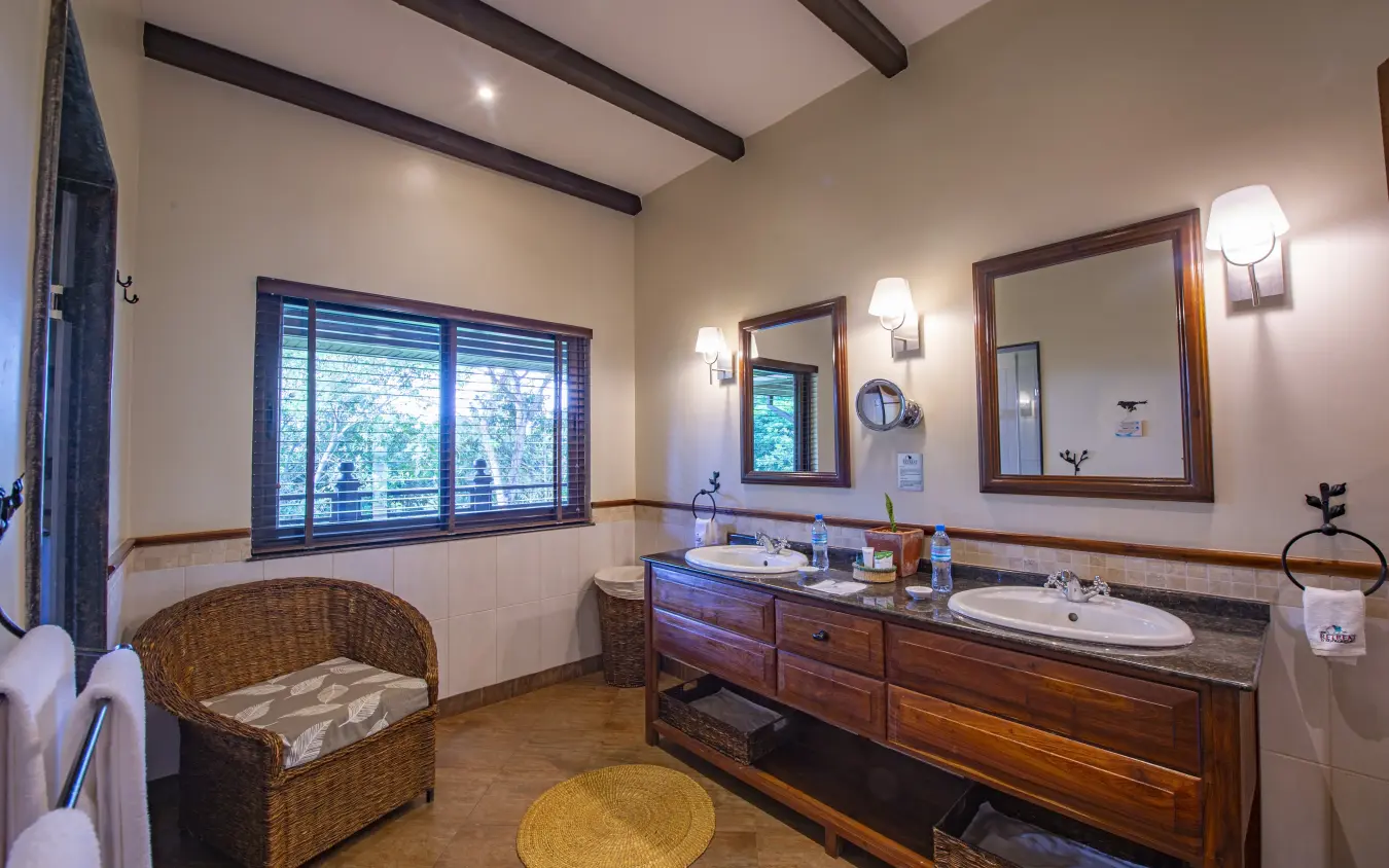 Luxury bathroom with dual vanity and wicker seating overlooking gardens, The Retreat at Ngorongoro, Ngorongoro Crater, Tanzania