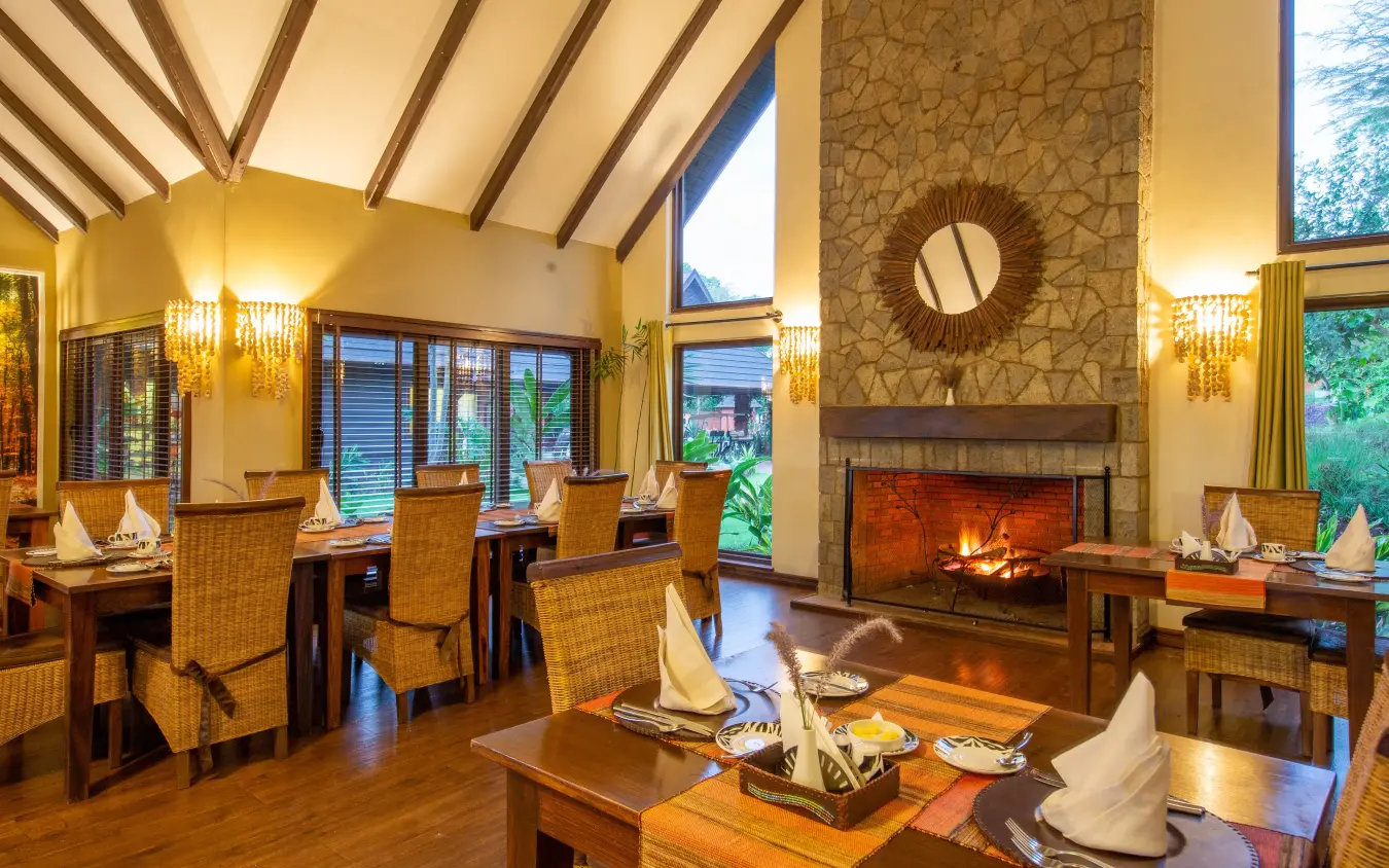 Luxury dining room with fireplace and wooden beam ceiling at dusk, The Retreat at Ngorongoro, Ngorongoro Crater, Tanzania