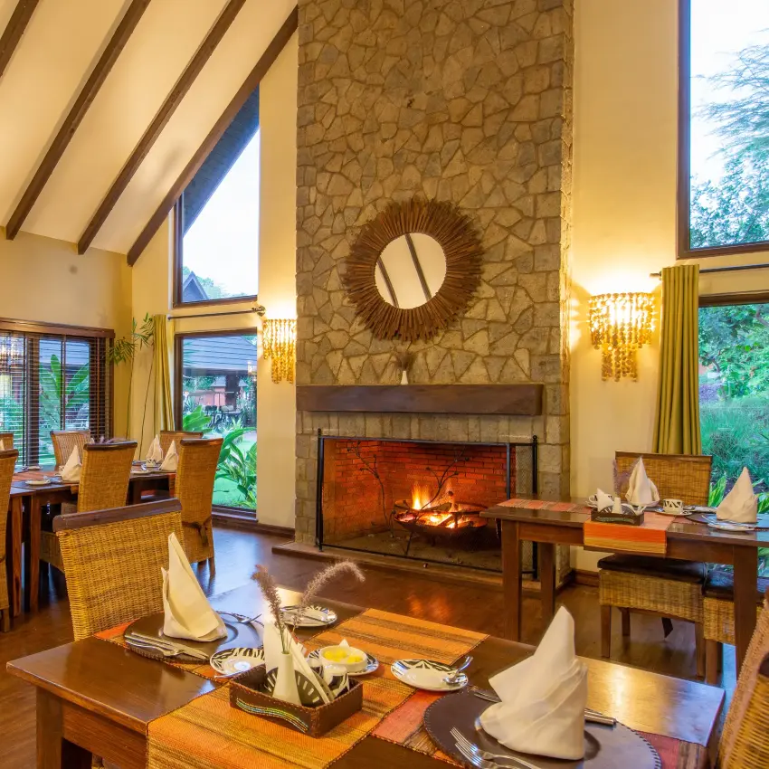 Luxury dining room with fireplace and wooden beam ceiling at dusk, The Retreat at Ngorongoro, Ngorongoro Crater, Tanzania