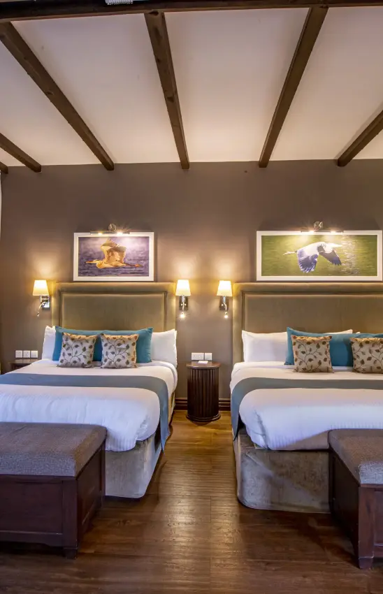 Twin beds in luxury lodge room with exposed wooden beams and framed wildlife art, The Retreat at Ngorongoro, Ngorongoro Crater, Tanzania