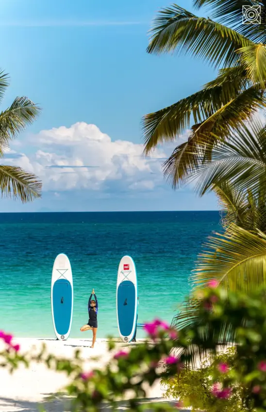 Woman standing between paddleboards on tropical beach, Zuri Zanzibar, Zanzibar & Pemba, Tanzania