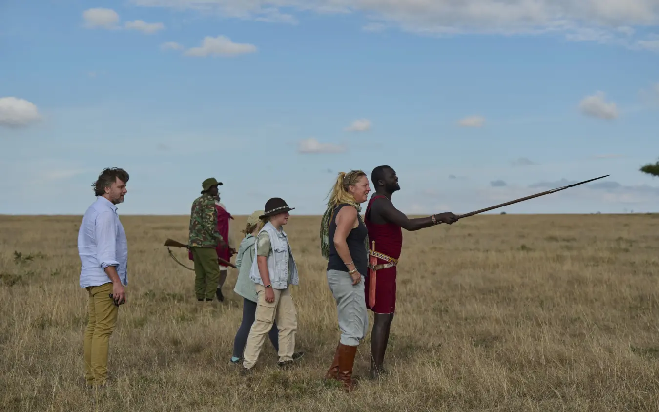 Maasai guide demonstrating traditional hunting technique with spear to guests in grassland, Basecamp Wilderness, Maasai Mara, Kenya