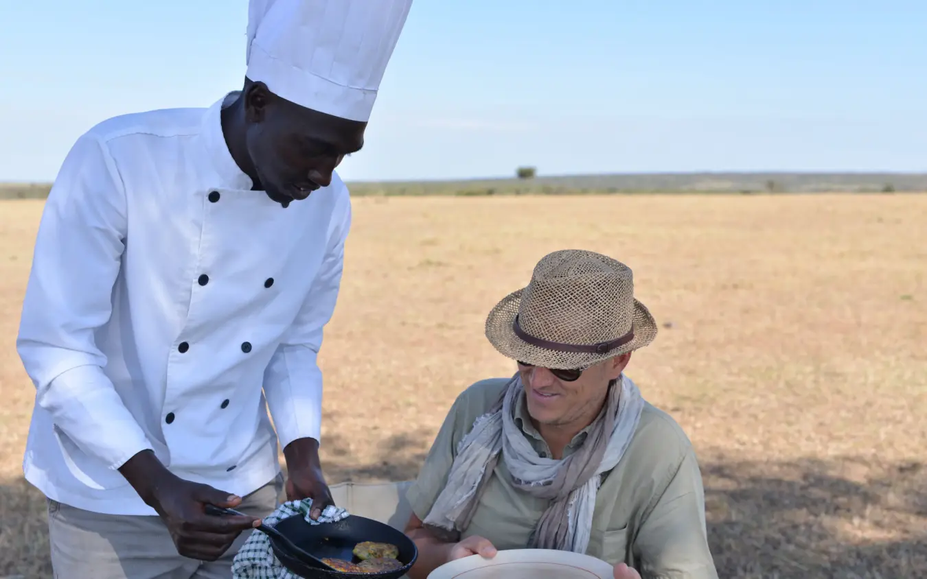 Chef serving meal to guest in vast arid landscape, Basecamp Wilderness, Maasai Mara, Kenya