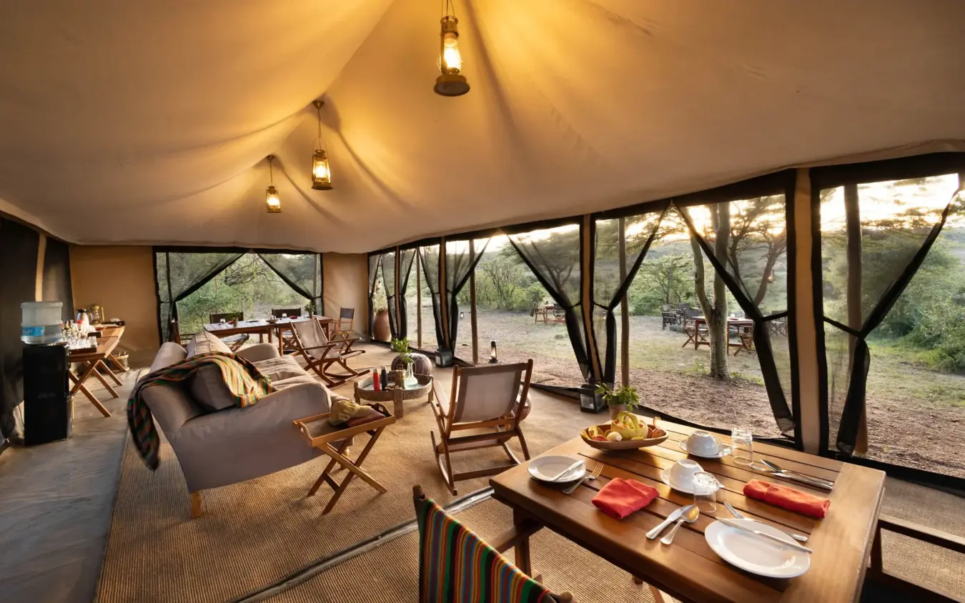 Luxury safari tent interior with dining area and savanna views through large windows, Basecamp Wilderness, Maasai Mara, Kenya