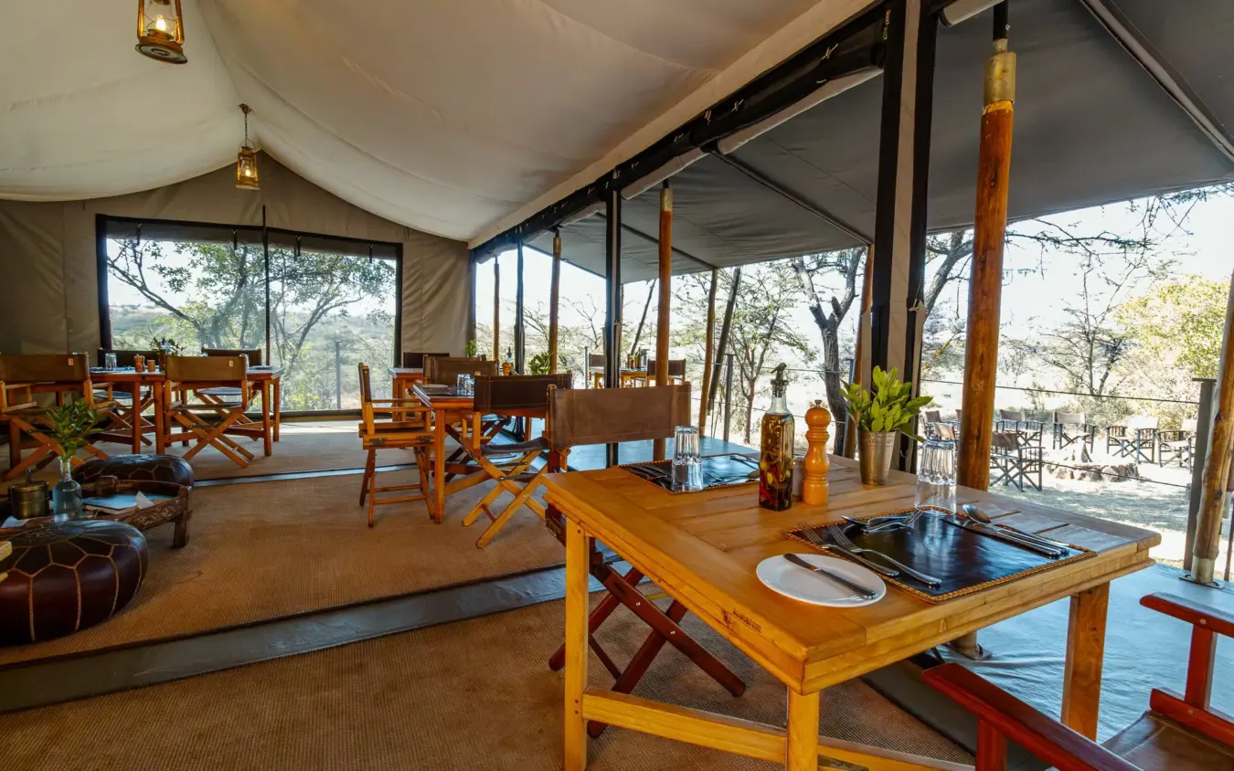 Safari lodge dining tent with wooden furniture and savanna views, Basecamp Wilderness, Maasai Mara, Kenya