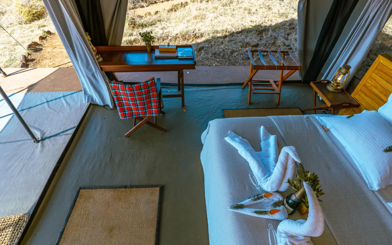 Glamping tent interior with bed overlooking rocky hillside and outdoor seating area, Basecamp Wilderness, Maasai Mara, Kenya