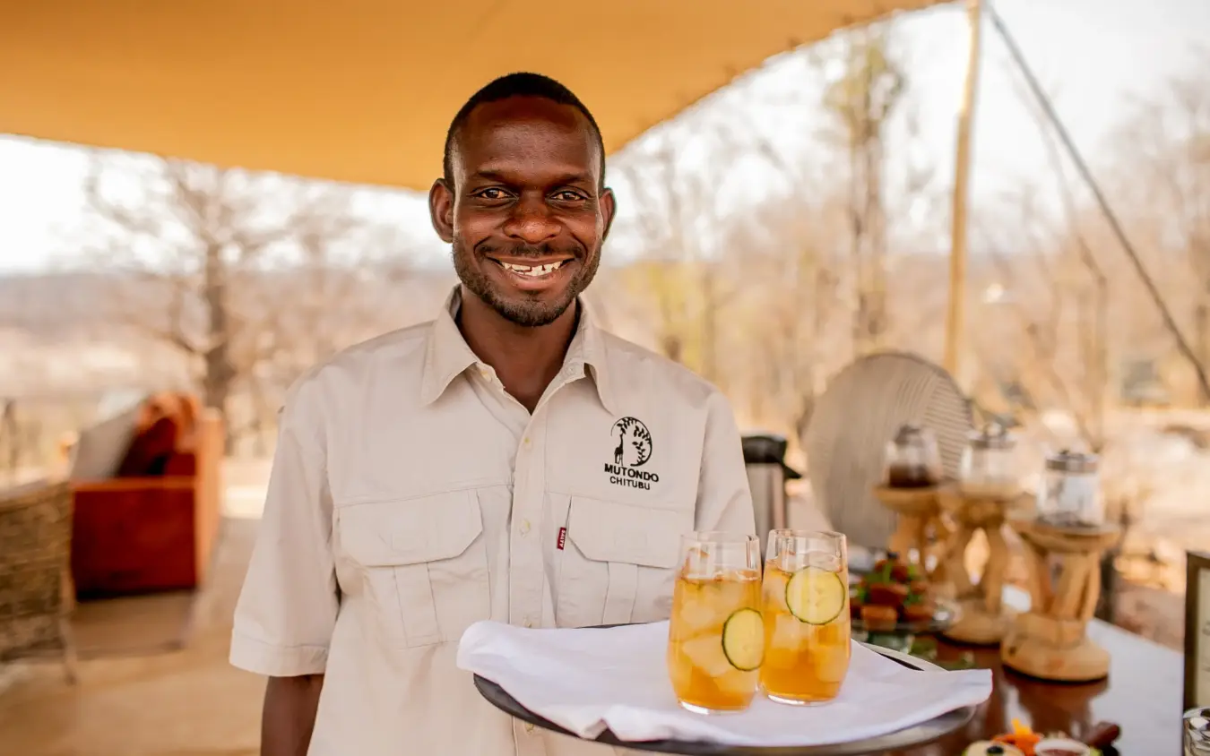 Smiling server with refreshing drinks under safari camp shade canopy, Camp Chitubu, Hwange National Park, Zimbabwe