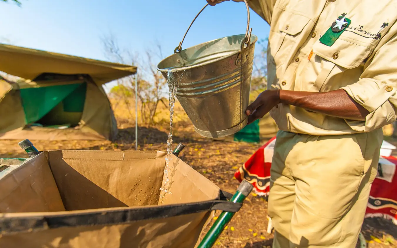Guide pouring water into container at safari camp, Delta Camp, The Okavango Delta, Botswana