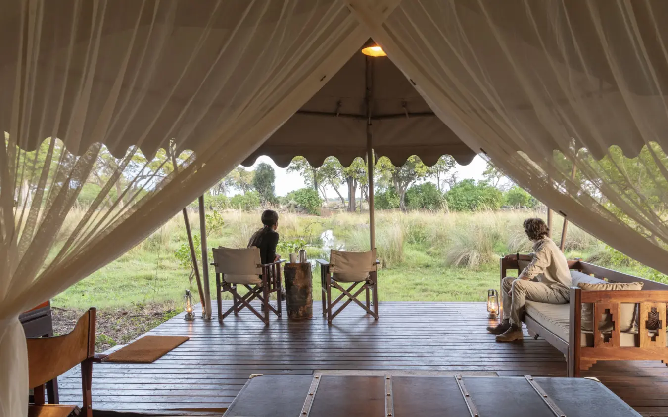 Luxury safari tent interior with guests overlooking savanna landscape, Duba Explorers Camp, The Okavango Delta, Botswana