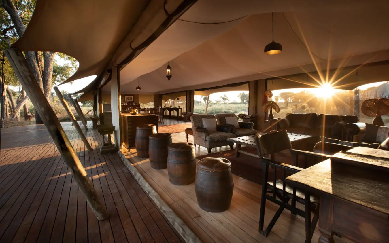 Open-air lodge lounge with wooden deck at sunset overlooking savanna landscape, Duba Explorers Camp, The Okavango Delta, Botswana