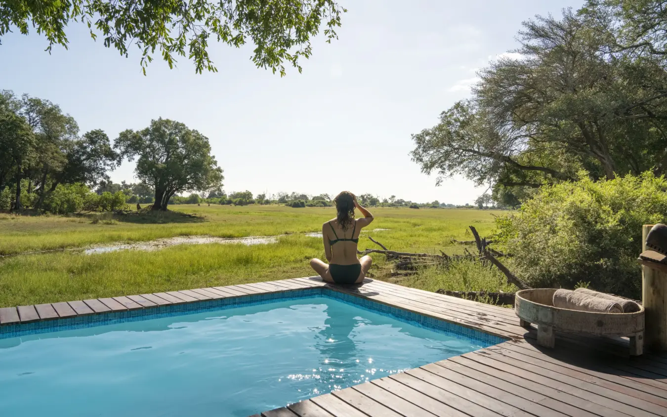 Woman relaxing by infinity pool overlooking floodplain landscape, Duba Explorers Camp, The Okavango Delta, Botswana