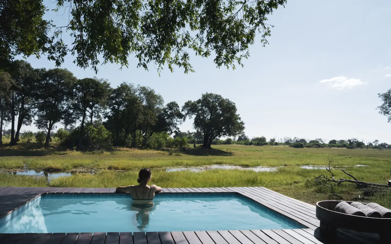 Guest relaxing in infinity pool overlooking wetland and acacia woodland, Duba Explorers Camp, The Okavango Delta, Botswana