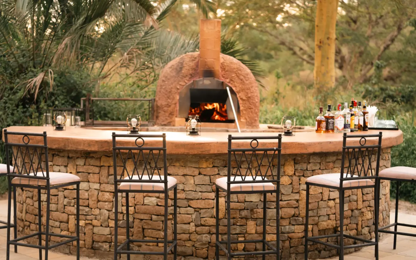 Outdoor stone bar with wood-fired pizza oven and seated guests among trees, The Emakoko, Nairobi, Kenya