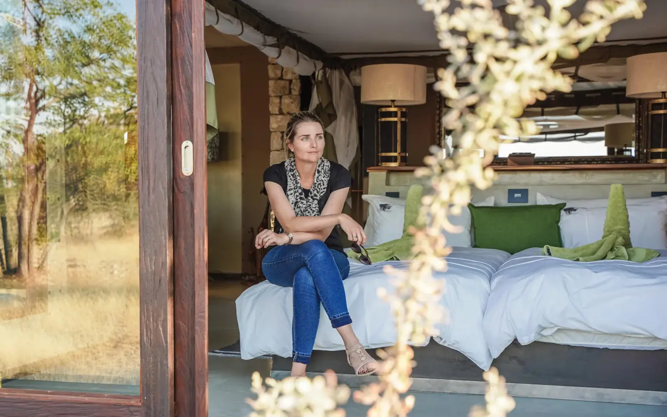 Woman sitting on bed in safari lodge room, Etosha Oberland Lodge, Etosha National Park, Namibia