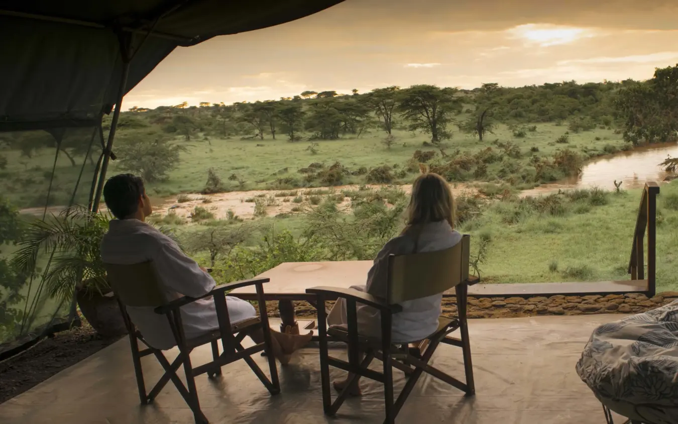 Guests seated at viewing platform overlooking river and savanna grassland, Hemingways River Camp Mara, Maasai Mara, Kenya