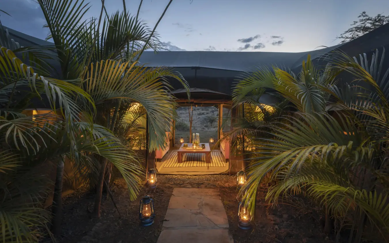 Candlelit outdoor pavilion with palm trees at dusk overlooking mountains, Hemingways River Camp Mara, Maasai Mara, Kenya
