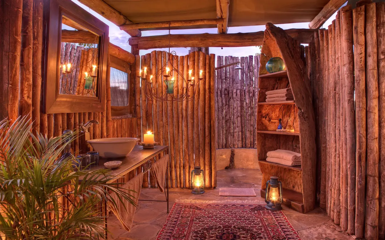 Rustic wooden lodge bathroom with carved details and warm lighting, Hemingways River Camp Mara, Maasai Mara, Kenya