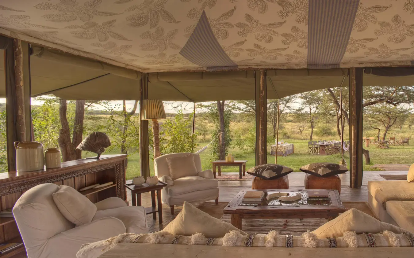 Open-sided safari lodge lounge with savanna views and wildlife visible in distance, Hemingways River Camp Mara, Maasai Mara, Kenya
