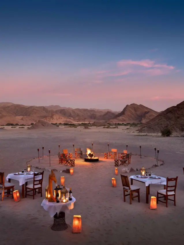 Candlelit dinner setup on desert sand at dusk with mountains beyond, Hoanib Valley Camp, Damaraland, Namibia