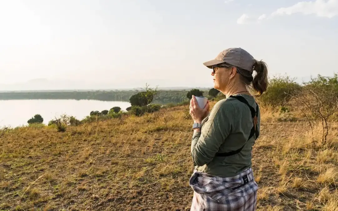 Guest observing wildlife across savanna landscape with water, Honey Bear Bush Camp, Queen Elizabeth NP, Uganda