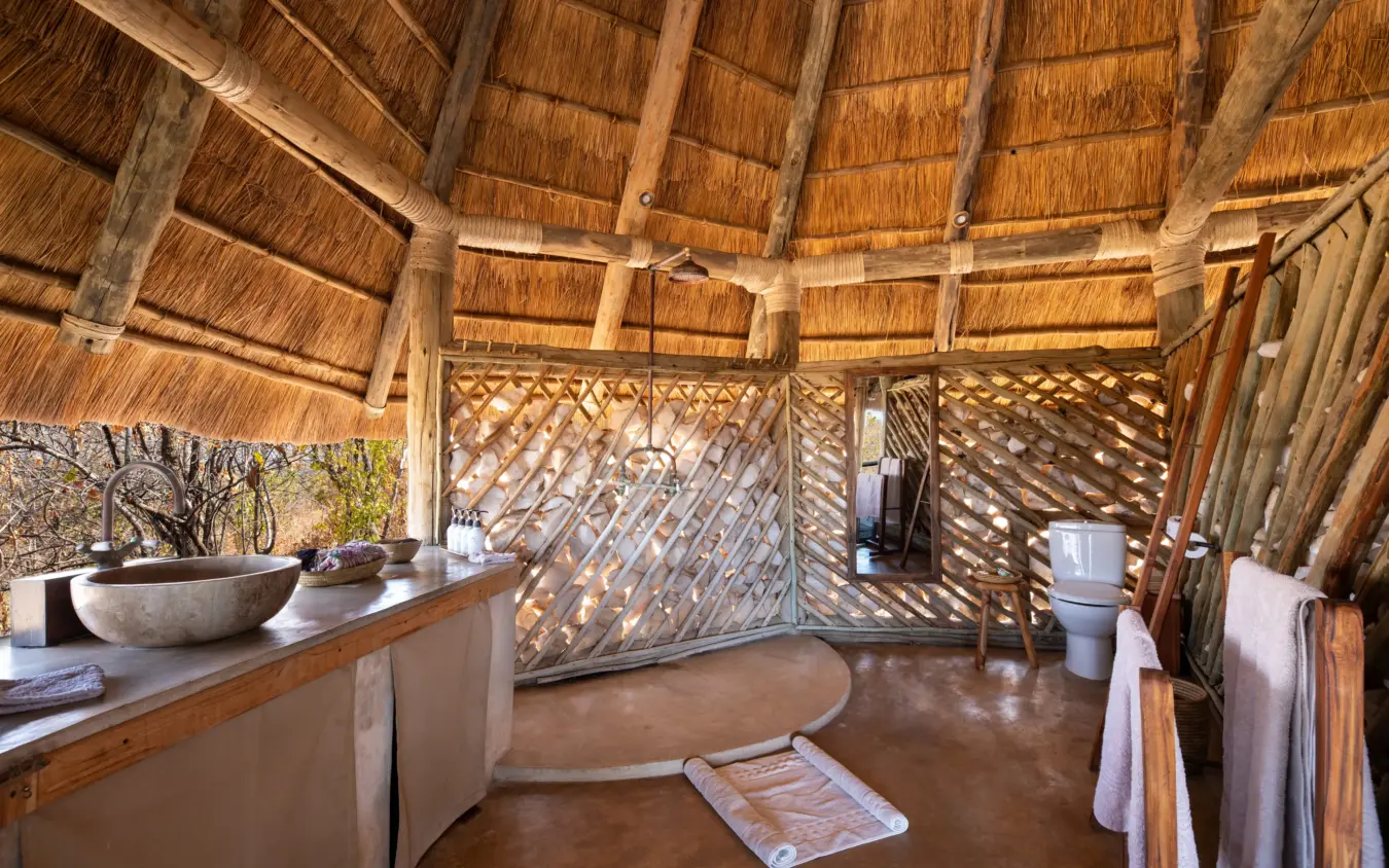 Interior of thatched safari lodge bathroom with stone basin and lattice doors, Ikuka Safari Camp, Ruaha National Park, Tanzania