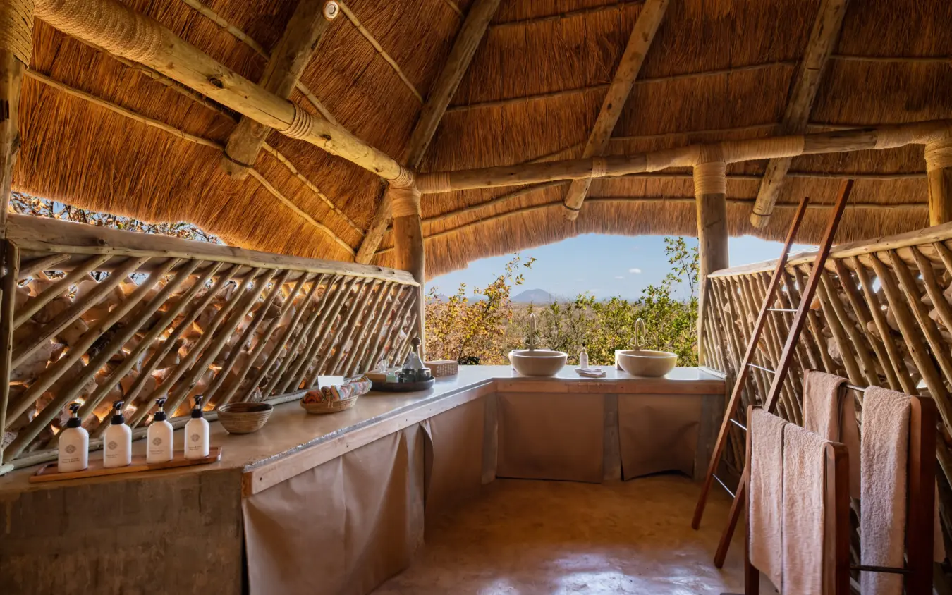Luxury spa bathroom with thatched roof overlooking savanna landscape, Ikuka Safari Camp, Ruaha National Park, Tanzania