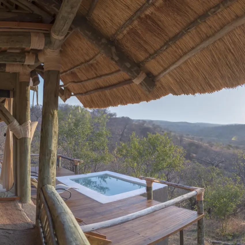 Wooden deck with plunge pool and thatched roof overlooking forested valley, Ikuka Safari Camp, Ruaha National Park, Tanzania