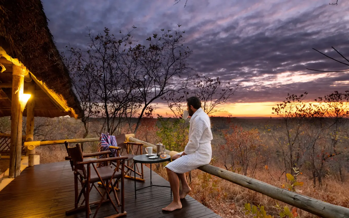 Man relaxing on wooden deck at sunset overlooking savanna landscape, Ikuka Safari Camp, Ruaha National Park, Tanzania