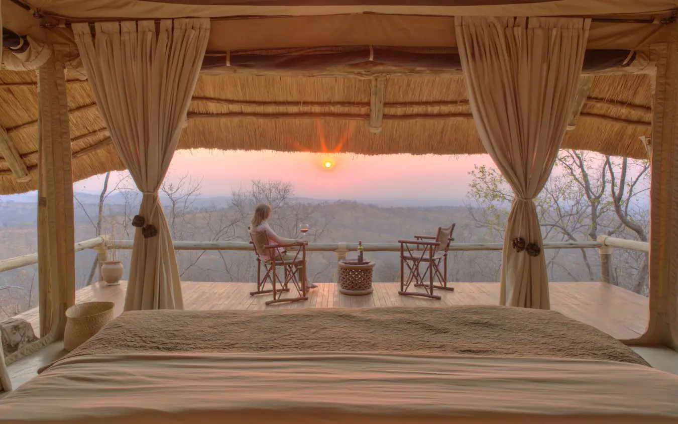 Woman relaxing on safari lodge deck at sunset overlooking savanna landscape, Ikuka Safari Camp, Ruaha National Park, Tanzania