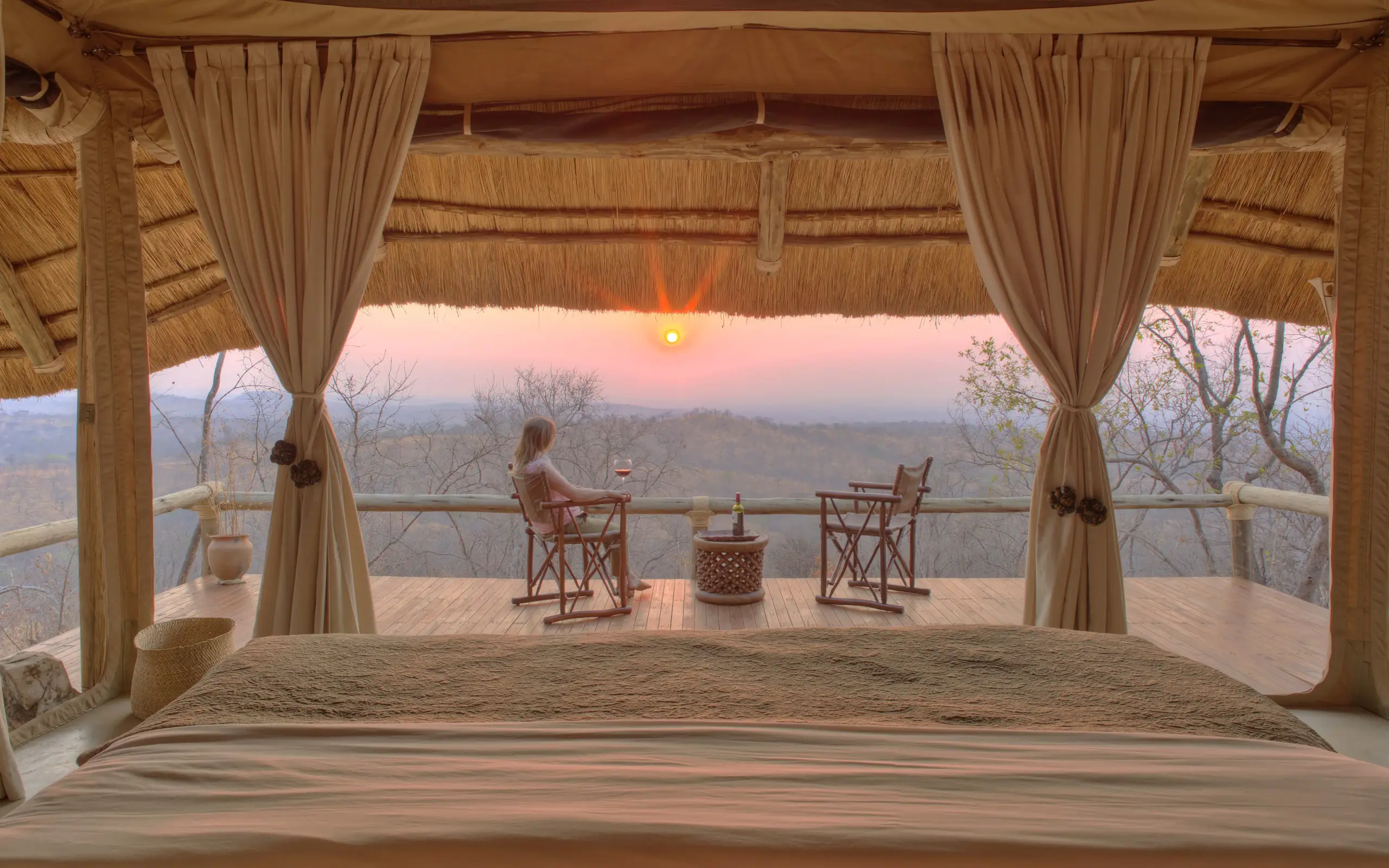 Woman relaxing on safari lodge deck at sunset overlooking savanna landscape, Ikuka Safari Camp, Ruaha National Park, Tanzania