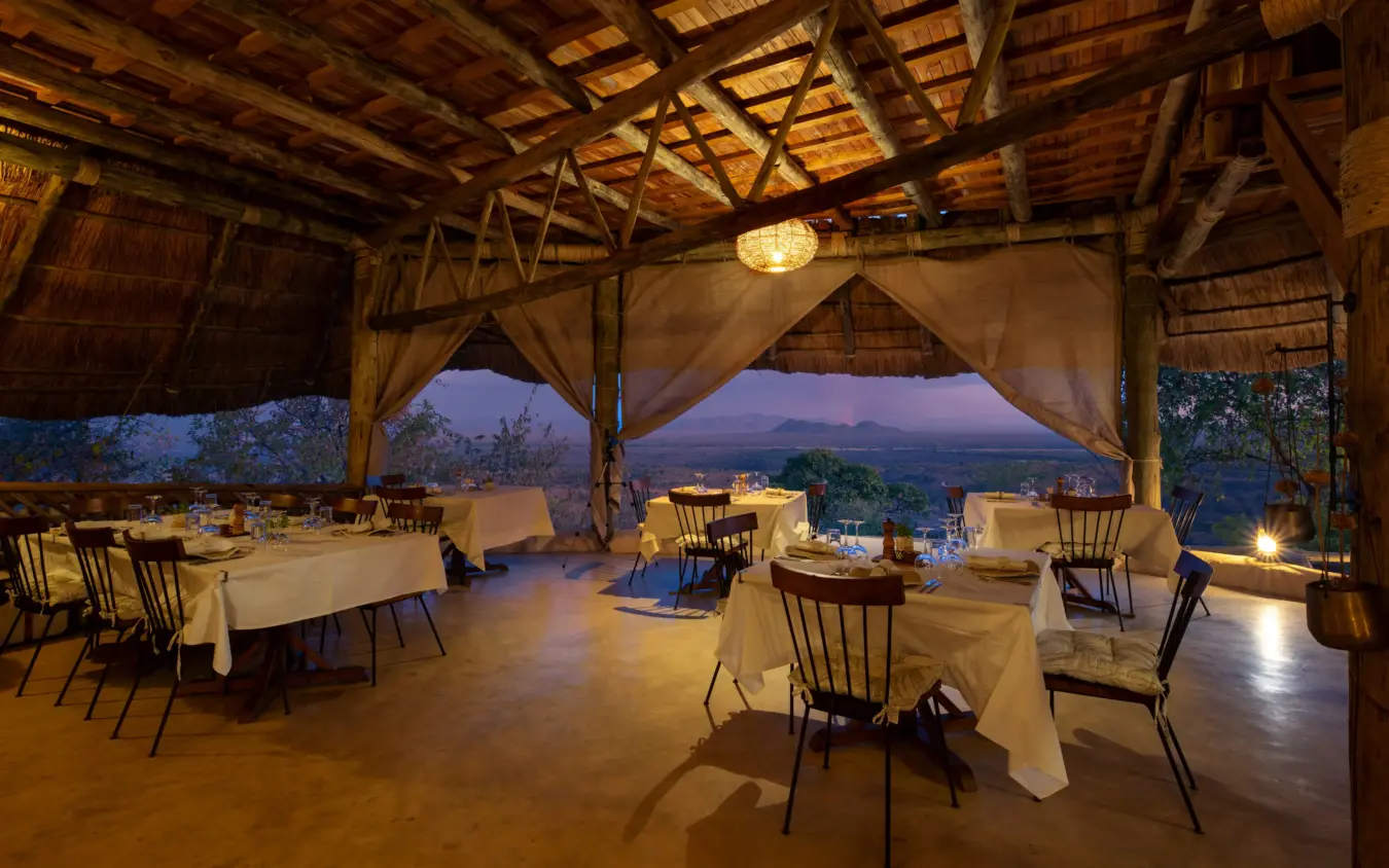 Open-air dining pavilion with candlelit tables overlooking valley at dusk, Ikuka Safari Camp, Ruaha National Park, Tanzania