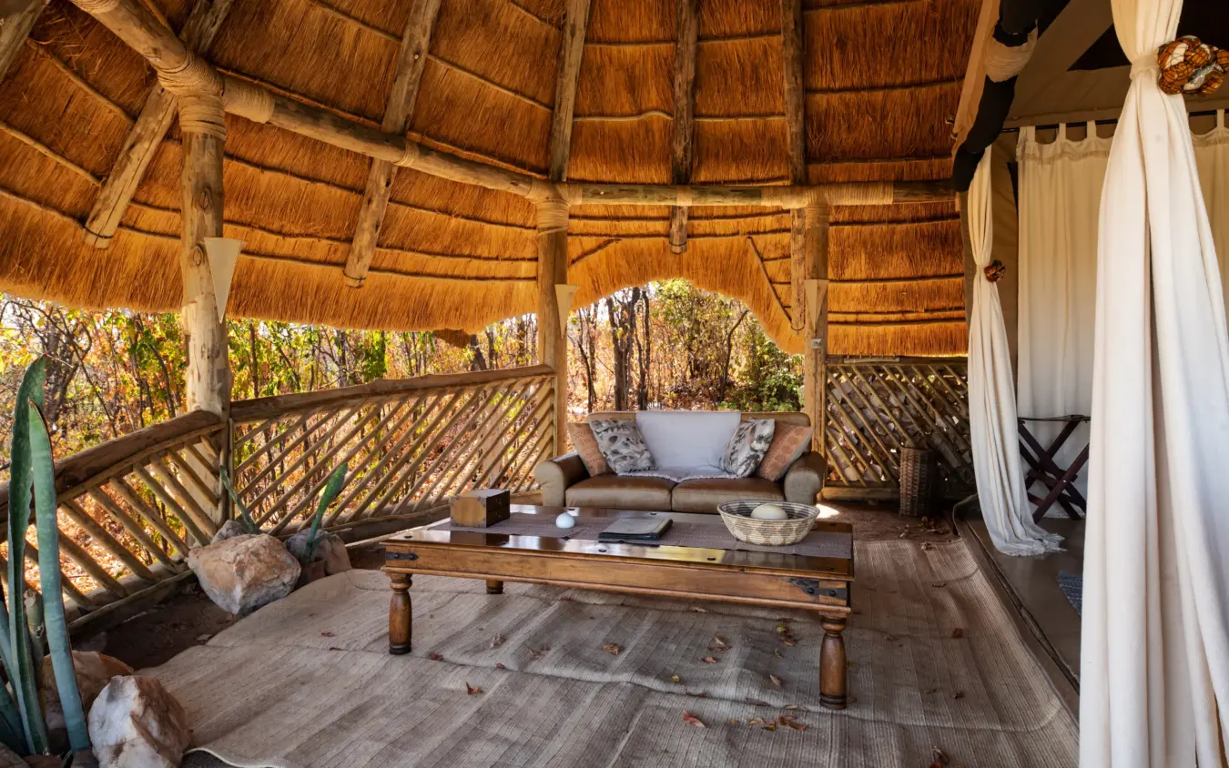 Thatched-roof lodge pavilion with wooden deck and safari furniture overlooking forest, Ikuka Safari Camp, Ruaha National Park, Tanzania