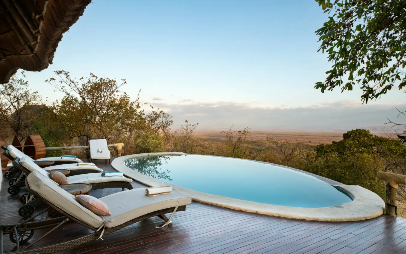 Infinity pool with loungers overlooking expansive savanna landscape at dusk, Ikuka Safari Camp, Ruaha National Park, Tanzania
