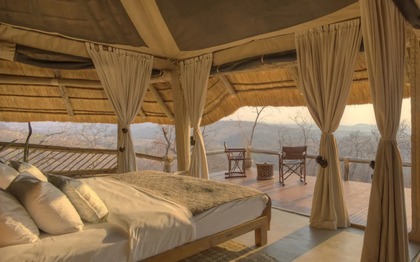 Luxury safari bedroom with draped curtains overlooking vast valley landscape, Ikuka Safari Camp, Ruaha National Park, Tanzania