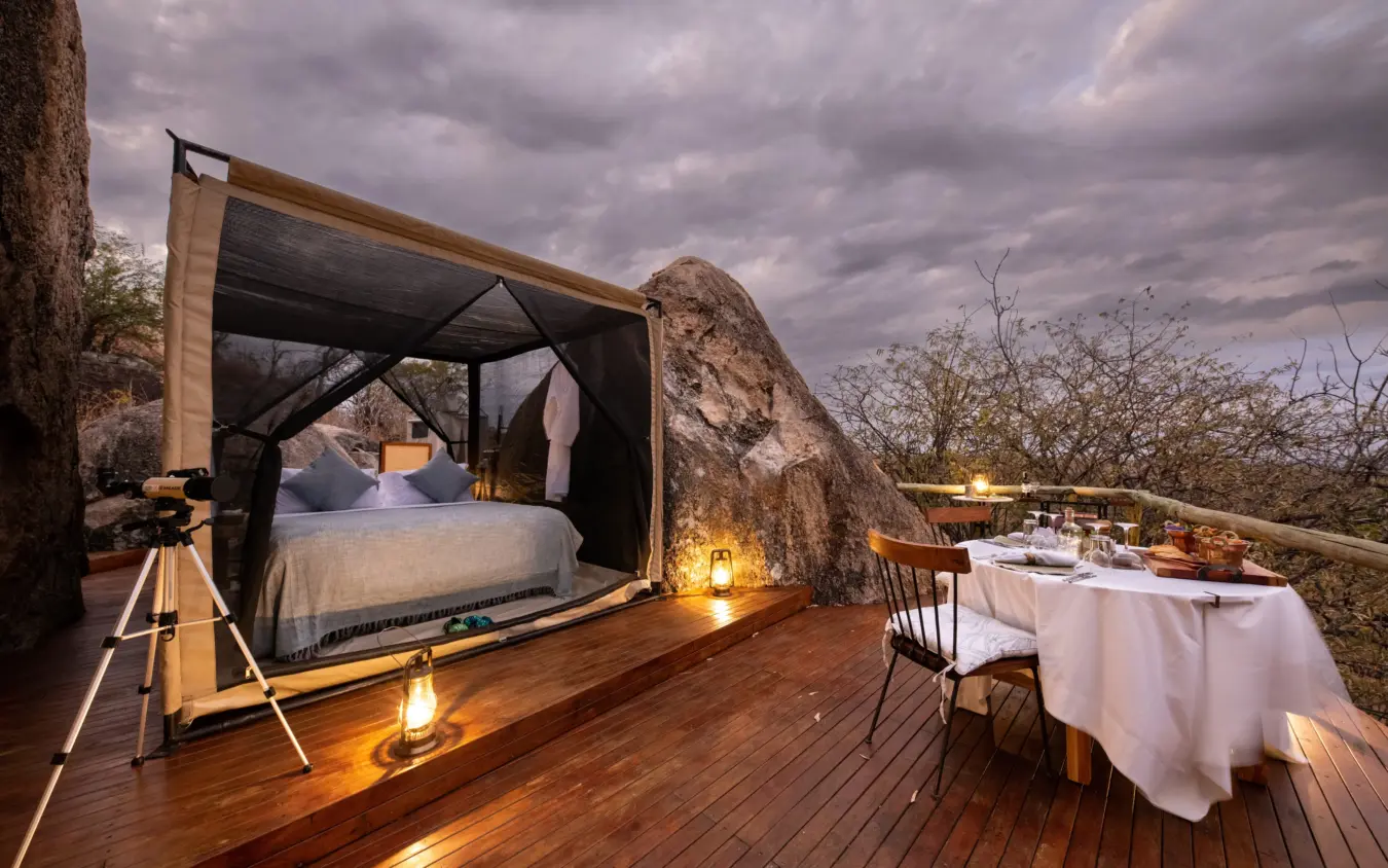 Luxury bedroom platform with natural rock formations at dusk, Ikuka Safari Camp, Ruaha National Park, Tanzania