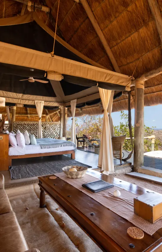 Thatched safari pavilion with bed and wooden furniture overlooking landscape, Ikuka Safari Camp, Ruaha National Park, Tanzania