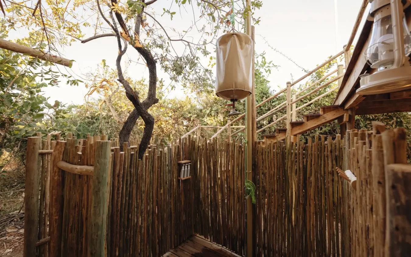 Outdoor shower enclosure with wooden walls beneath acacia tree, Kigelia Ruaha, Ruaha National Park, Tanzania