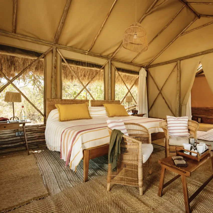 Safari tent interior with bed and woven furnishings overlooking savanna, Kigelia Ruaha, Ruaha National Park, Tanzania